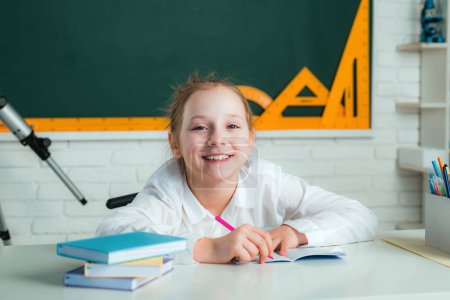 Foto de Chica con expresión de cara feliz cerca de escritorio con útiles escolares - Imagen libre de derechos