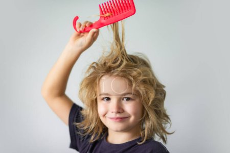 Photo for Funny kids hairstyle. Child with tangled blonde long hair tries to comb it. Hair portrait kid with a comb - Royalty Free Image