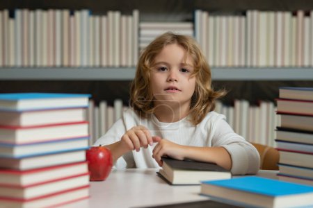 Photo for Kid nerd pupil reads books in the library. Schoolboy with book in class. Literature for reading. Child learning from books. School education and clever talented little genius - Royalty Free Image