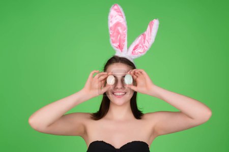 Téléchargez les photos : Easter girl. Lovely young woman in rabbit ears celebrating easter holiday, studio background. Holidays party concept. Cheerful girl celebrating Easter in rabbit ears, holding painted eggs - en image libre de droit