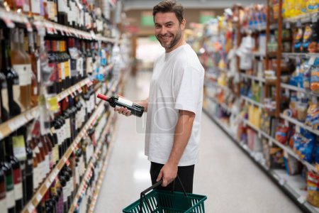 Photo for Handsome man with shopping basket with grocery. Man choosing alcohol bottles at liquor store - Royalty Free Image