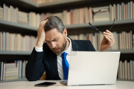 Photo for Millennial Businessman in office having headache. Business man in suit work on laptop at home office take off glasses suffer from migraine or headache. Tired exhausted man suffering from headache - Royalty Free Image