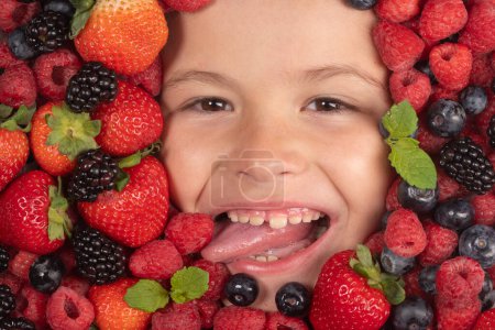 Téléchargez les photos : Des fruits drôles. Visage enfant aux baies mélange de fraises, bleuets, framboises, mûres - en image libre de droit