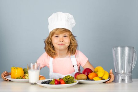 Téléchargez les photos : Portrait de chef enfant en chapeau de cuisinier. Cuisson à la maison, gamin préparant des aliments à partir de légumes et de fruits. Une alimentation saine - en image libre de droit