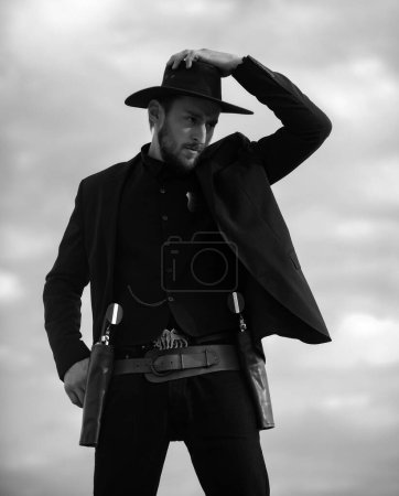Photo for Sheriff in black suit and cowboy hat. Wild west, western, man with vintage pistol revolver and marshal ammunition - Royalty Free Image