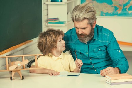Photo for Cute child boy with teacher in classroom near blackboard desk. Home school for pupil. Cute pupil and his father schooling work - Royalty Free Image