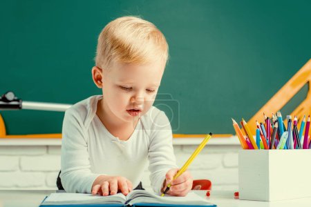 Téléchargez les photos : Petit garçon mignon dans la salle de classe près du bureau du tableau noir. Espace de copie de tableau. Processus éducatif - en image libre de droit