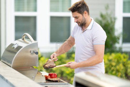 Photo for Man cooking meat on barbecue in the backyard of the house. Handsome man preparing barbecue. Barbecue chef master. Cook preparing delicious grilled barbecue food, bbq meat. Grill and barbeque - Royalty Free Image