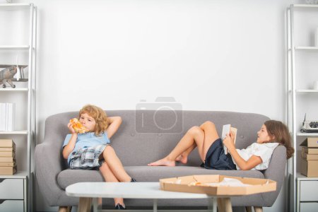 Foto de Dos niños pequeños comiendo pizza en casa. Niños hambrientos comiendo pizza. Pizza de pepperoni para niños. Niños sosteniendo una rebanada de pizza en la fiesta en casa - Imagen libre de derechos