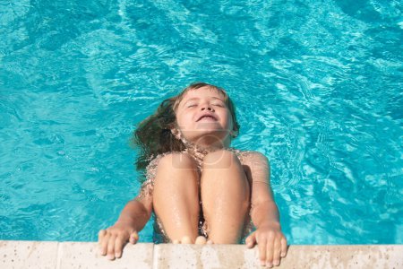 Téléchargez les photos : Enfant dans la piscine d'été. Joyeux petit garçon jouant avec dans la piscine extérieure par une chaude journée d'été. Les enfants apprennent à nager. Vacances familiales à la plage - en image libre de droit