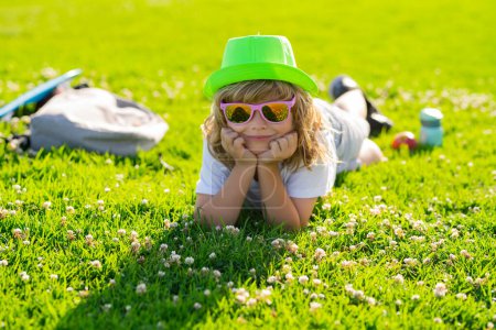 Téléchargez les photos : Enfant garçon mignon profiter de se détendre sur la pelouse. Détendez-vous au parc d'été. Garçon enfant couché sur l'herbe verte en plein air - en image libre de droit
