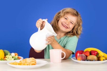 Téléchargez les photos : Un enfant boit du lait. Mignon enfant boire du lait sur fond bleu - en image libre de droit