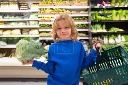 Foto de Child with cabbage. Kid is choosing fresh vegetables and fruits in the store. Child buying food in grocery supermarket - Imagen libre de derechos