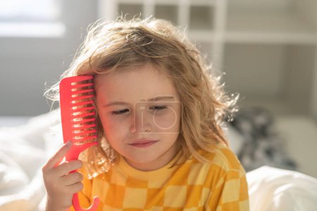 Photo for Boy brushes his hair. Child with tangled blonde long hair tries to comb it. Hair portrait kid with a comb - Royalty Free Image