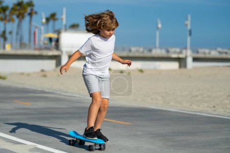 Foto de Young boy on his skateboard striking and practices his skill at the skate park. Happy child having fun on summer holidays. Pretty little kid learning to skateboard outdoors on beautiful summer day - Imagen libre de derechos