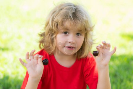 Photo for Happy little child hold cherry ner face. Child eat cherries in the summer. Kid is picking cherries in the garden - Royalty Free Image
