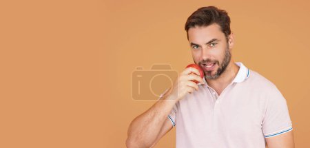 Téléchargez les photos : Un homme mordant de délicieuses pommes rouges. Homme mangeant des pommes, portrait en studio. Petit déjeuner matinal. Homme avec des dents saines tenant des pommes sur fond isolé jaune beige. Homme tenant une pomme - en image libre de droit
