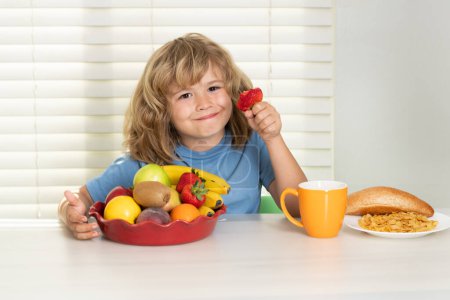 Foto de Niño con fresa, frutas de verano. Niño comiendo alimentos saludables vegetales. Desayuno con leche, frutas y verduras. Niño comiendo durante el almuerzo o la cena - Imagen libre de derechos