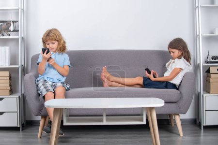 Photo for Children alone with phone home. Happy cheerful kids watching media on smartphone, making video call to parent, playing online game, using internet. Parental control, social media addiction. Bad habit - Royalty Free Image