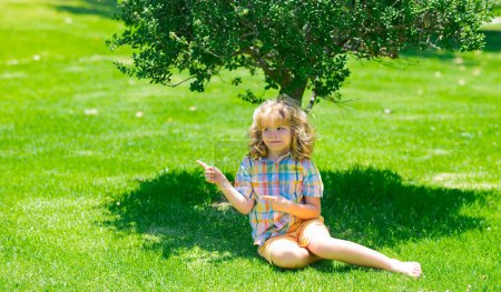 Téléchargez les photos : Vacances d'été avec les enfants. Détendez-vous au parc d'été. Enfant assis sur l'herbe verte en plein air. Pique-nique d'été sur herbe avec enfants - en image libre de droit