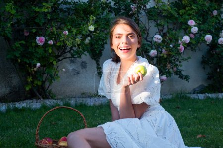 Photo for Excited amazed woman bitting apple, healthy lifestyle. Girls holds a fresh green apple outdoor portrait on spring park. Healthy food. Fruit for healthy teeth. Woman eat apple - Royalty Free Image