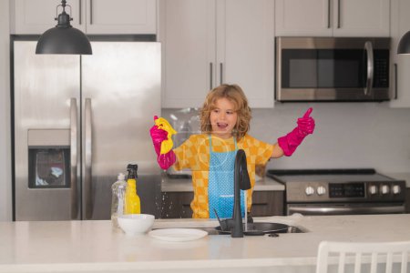 Foto de Platos limpios. Lindo niño ayudando con el hogar, limpiando platos en la cocina. Adorable ayudante de limpieza infantil. Pequeño niño lindo barrer y limpiar los platos en la cocina - Imagen libre de derechos