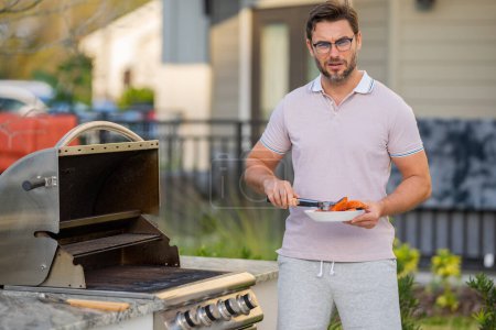Photo for Man cooking meat on barbecue in the backyard of the house. Handsome man preparing barbecue salmon fillet. Barbecue chef master. Cook preparing delicious grilled barbecue food, bbq salmon fillet - Royalty Free Image