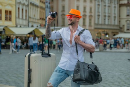 Téléchargez les photos : Voyageur homme avec lunettes de soleil, chapeau et appareil photo. Voyageur homme touriste voyageant à l'étranger pour voyager le week-end escapade. Homme allant en vacances tenant bagages sac de voyage en plein air - en image libre de droit