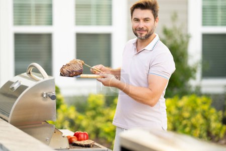 Photo for Barbecue master. Middle aged hispanic man in apron for barbecue. Roasting and grilling food. Man hold cooking utensils barbecue. Roasting meat outdoors. Barbecue and grill. Cooking meat in backyard - Royalty Free Image