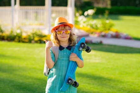 Téléchargez les photos : Happy boy laughing and holding skateboard outdoor. Summer fashion kids portrait - en image libre de droit