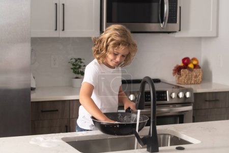 Téléchargez les photos : Les corvées domestiques. Enfant dans des plaques de nettoyage de cuisine. Mignon garçon qui lave la vaisselle dans la cuisine domestique. Enfant garçon laver la vaisselle dans l'évier de la cuisine - en image libre de droit
