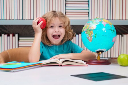 Foto de Niño de escuela con libros y manzana en la biblioteca. Un niño de la escuela. Retrato de estudiante nerd con útiles escolares - Imagen libre de derechos