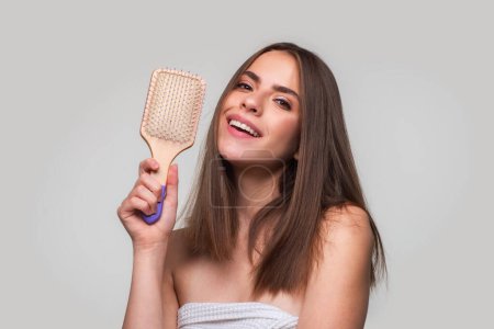 Téléchargez les photos : Femme souriante brossant les cheveux avec un peigne. Belle fille peigner les cheveux longs avec une brosse à cheveux - en image libre de droit