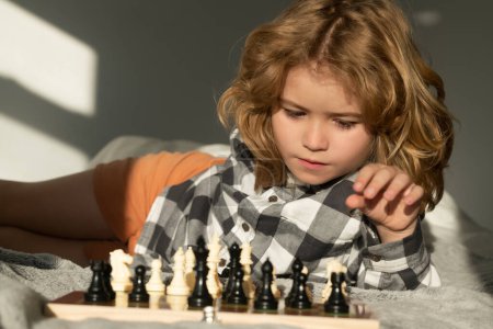 Téléchargez les photos : Mignon enfant jouant aux échecs à la maison. Un gamin qui pense aux échecs. Le concept d'apprentissage et de croissance des enfants. Échecs, succès et victoire. Jeu de logique de plateau, passe-temps des enfants et mode de vie - en image libre de droit