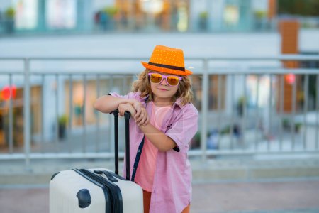 Foto de Un viajero pequeño con maleta. Niño viajero sosteniendo maleta al aire libre. Turista chico teniendo alegre viaje de vacaciones - Imagen libre de derechos