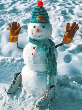Téléchargez les photos : Mignon petit bonhomme de neige en plein air. Le bonhomme de neige porte un chapeau et une écharpe en fourrure. Bonhomme de neige en plein air. Bonhomme de neige isolé sur fond de neige. Bonhomme de neige dans un foulard et un chapeau - en image libre de droit