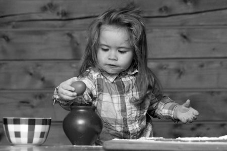 Téléchargez les photos : Petit garçon dans la cuisine cuisiner, jouer avec des œufs. Nourriture pour bébé, petits déjeuners en famille, jeux d'enfants avec les ustensiles de cuisine. Enfant bébé garçon pour casser l'oeuf - en image libre de droit
