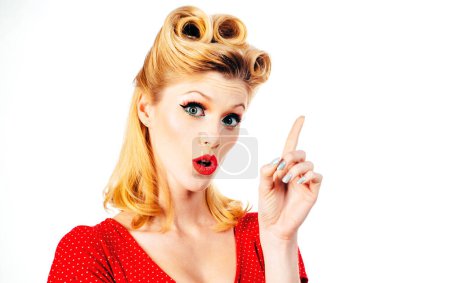 Photo for Portrait of beautiful young surprised woman, dressed in red pin-up dress. Caucasian blond model posing in retro fashion concept. Looking camera, showing pointing, copyspace. Thinking, daydreaming - Royalty Free Image