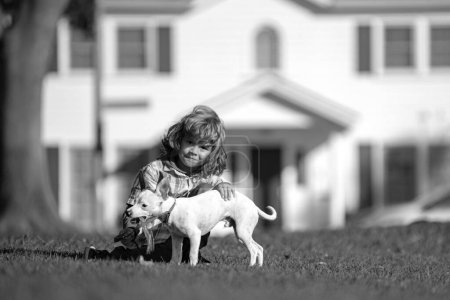 Foto de El niño abraza cariñosamente a su perro mascota. Feliz niño jugando con el cachorro en el jardín - Imagen libre de derechos