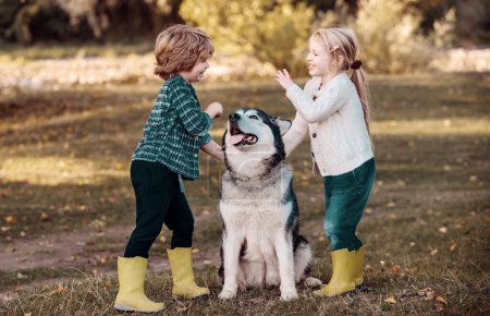 Foto de Niños sonrientes con perro paseando sobre el fondo del campo de otoño. Los niños abrazan amorosamente a su perro mascota. Recuerdos de la infancia - Imagen libre de derechos