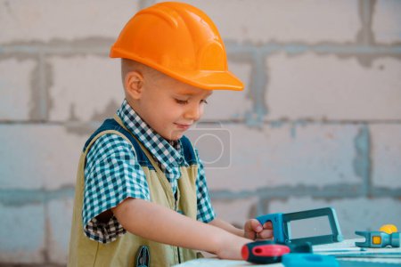 Téléchargez les photos : Portrait de petit constructeur en hardhats avec des instruments de rénovation sur la construction. Garçon constructeur, enfant charpentier avec ensemble d'outils constructeur - en image libre de droit