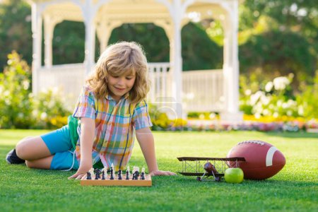 Téléchargez les photos : Un petit enfant joue aux échecs, échec-mat. Enfant jouant aux échecs à Spring Park. Enfant jouant aux échecs et s'amusant en plein air sur le jardin ou le parc d'été - en image libre de droit