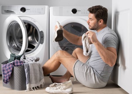 Photo for Man doing laundry at home near washing machine. Husband man doing laundry at home. Sexy guy washer putting clothes in the washing machine. Household concept. Washer and dryer, laundromat - Royalty Free Image