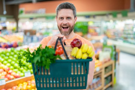 Téléchargez les photos : Homme avec panier plein de légumes et de fruits. Homme d'un millénaire d'âge moyen dans un magasin d'alimentation. Supermarché et concept d'épicerie. Homme homme 40s avec panier - en image libre de droit
