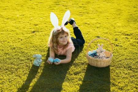 Photo for Easter kids boy in bunny ears hunting easter eggs outdoor. Cute child in rabbit costume with bunny ears having fun in park - Royalty Free Image