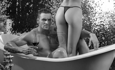Téléchargez les photos : Couple dans le bain. Homme sexy dans le bain boire du vin rouge. Style de vie luxueux. Homme avec femme dans la salle de bain. Torse masculin nu musculaire - en image libre de droit
