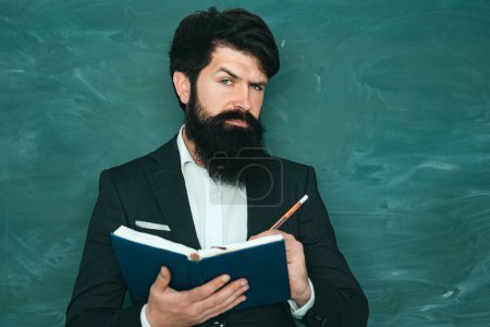 Téléchargez les photos : Étudiant masculin sérieux étudiant à l'école. Jeune professeur barbu près du tableau dans la classe de l'école. Professeur barbu à la leçon d'école aux bureaux dans la salle de classe - en image libre de droit