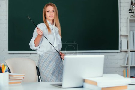 Photo for Young teacher with pointer on blackboard with copy space. Portrait of a young, confident and attractive female student studying in school classroom - Royalty Free Image