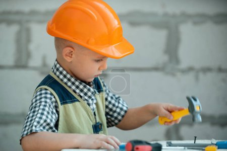 Photo for Kid in hard hat holding hammer. Little child helping with toy tools on construciton site. Kids with construction tools. Kids builder and repair construction worker - Royalty Free Image