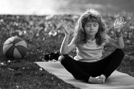Foto de Niño practicando yoga, ejercitándose usando ropa deportiva, camiseta al aire libre. Niños meditando durante el yoga. Niño meditando en pose de loto. Gimnasia, meditación para niños - Imagen libre de derechos